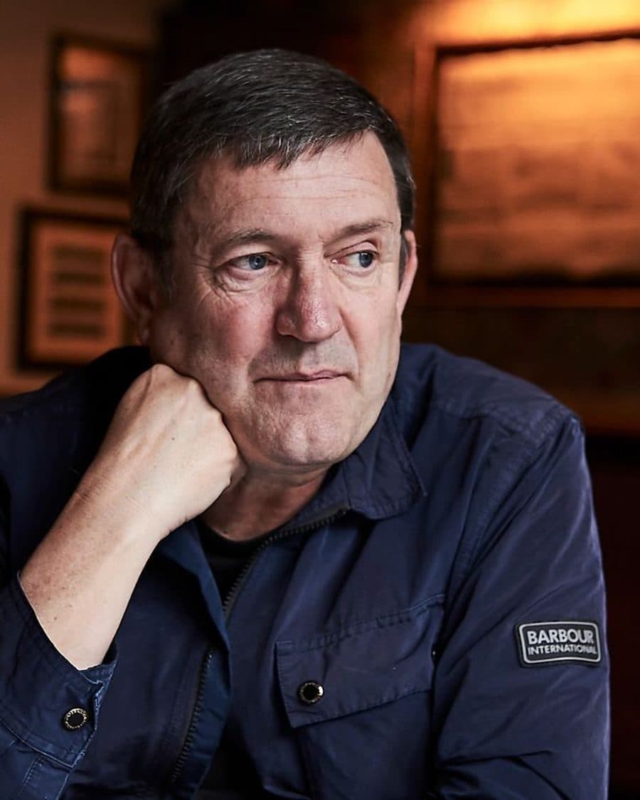 Paul Heaton in a navy jacket resting his chin on his hand in a pub snug - the official artist image