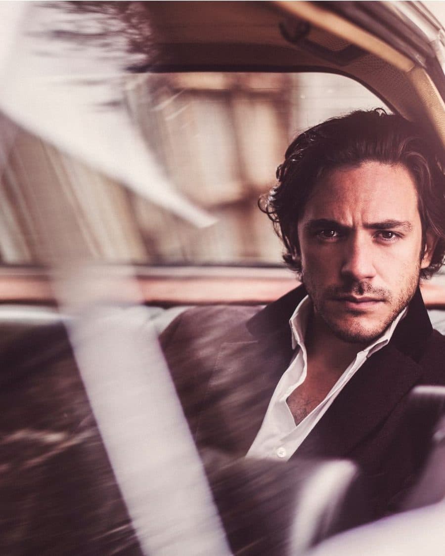 Jack Savoretti in a dark jacket and open white shirt looking out of a vintage car's rear window - the official artist image