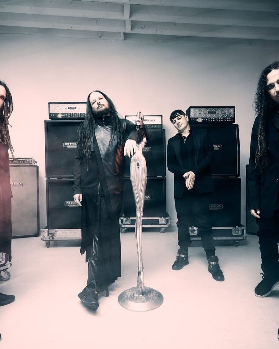 Korn's four members in black standing among stacked amp cabinets in a smoky white room - the official band image