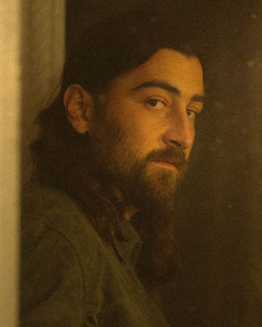 Noah Kahan in a doorway lit by a warm lantern, the official tour image