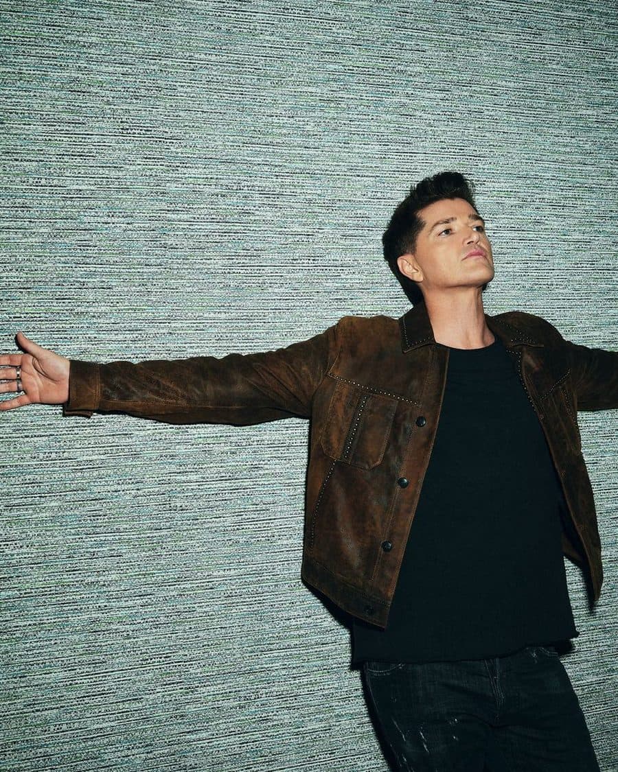 Danny O'Donoghue of The Script with arms outstretched in a brown suede jacket against a teal wall, the official tour image