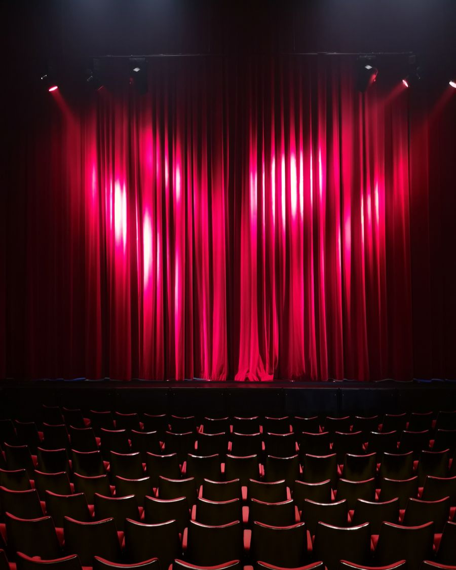 Theatre stage with dramatic red curtain and empty seats