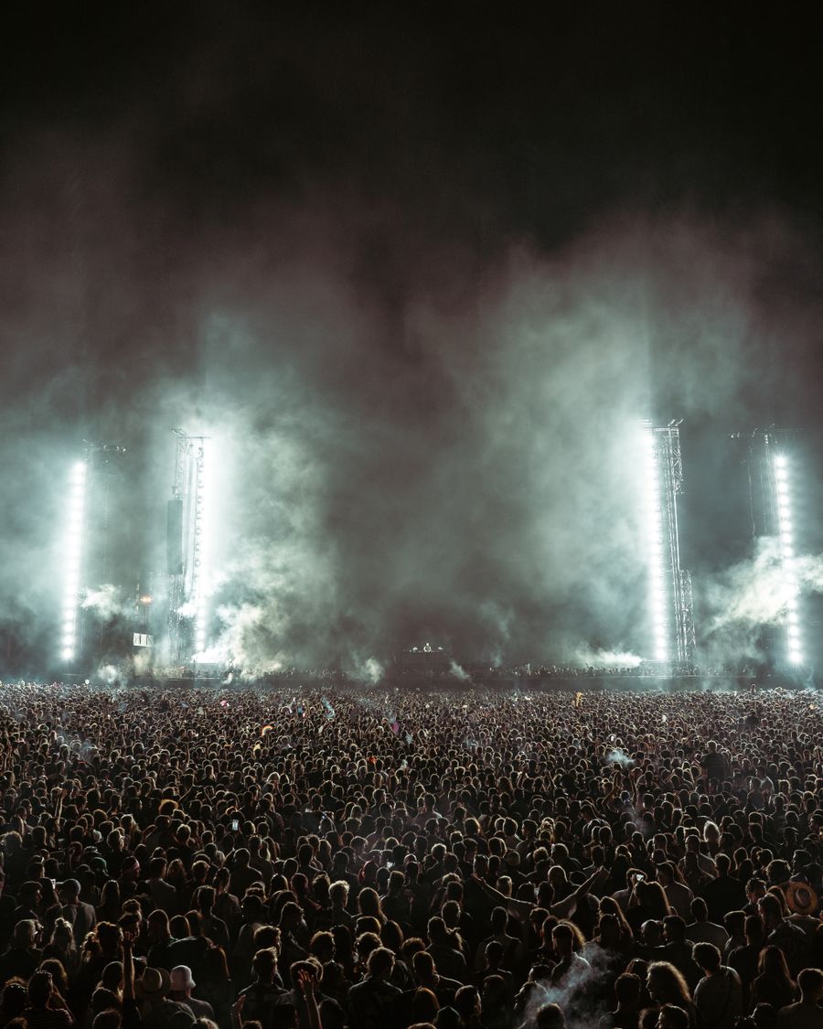 Vast stadium crowd facing a stage under white light columns
