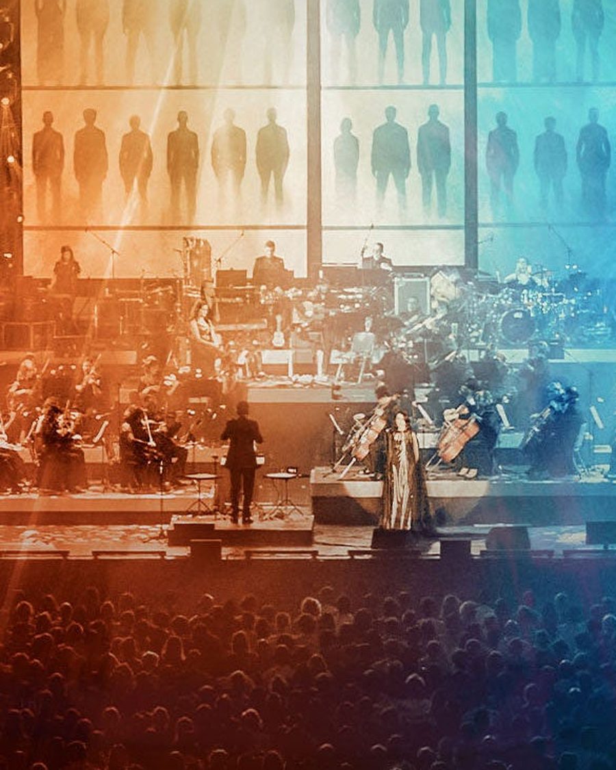 Orchestra and conductor on a stage lit red and blue, from The World of Hans Zimmer artwork - the official show image
