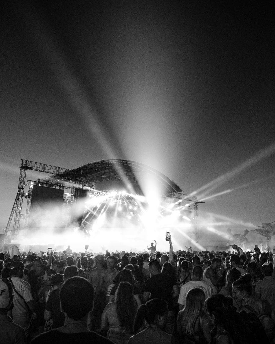 Black-and-white outdoor stage with sweeping searchlights