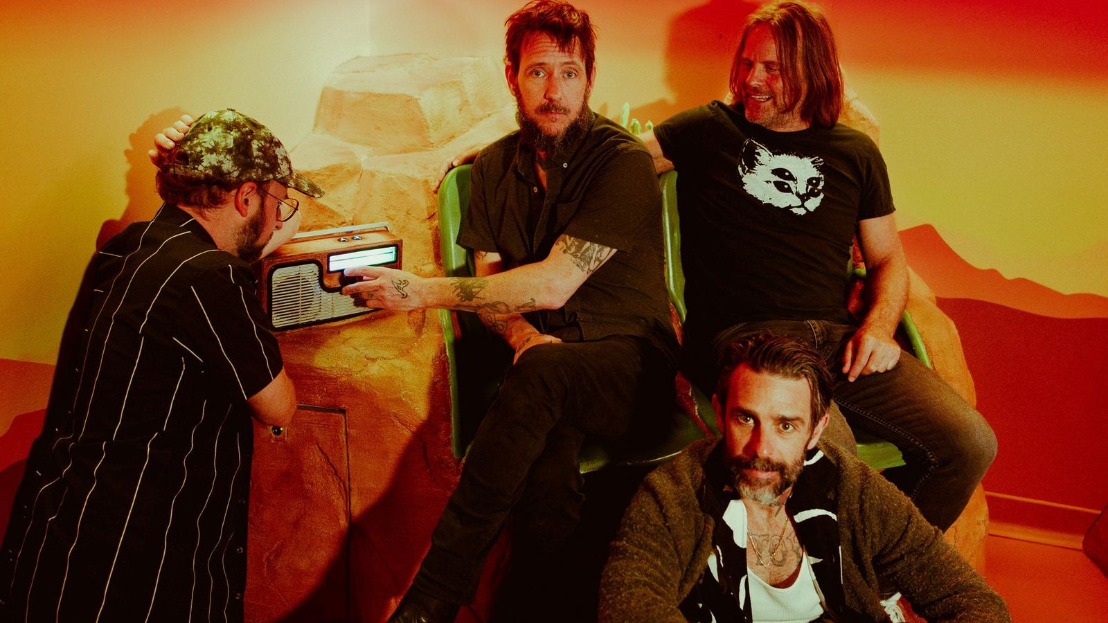 Band of Horses, four men around a wooden radio in a warm orange-lit room, the official band photo