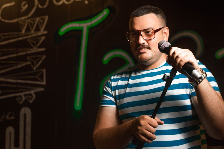 A stand-up comedian performing with a microphone under a single spotlight