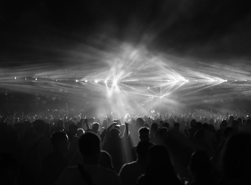 A black-and-white concert crowd under sweeping stage lights