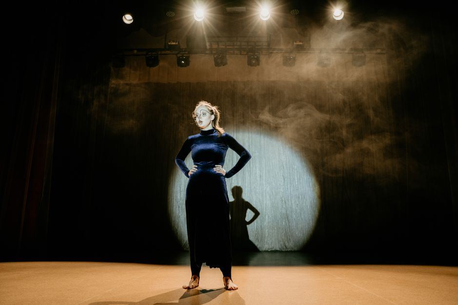 A performer silhouetted under a single stage spotlight