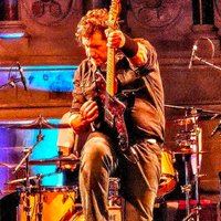 The Rising's frontman performing live with guitar under warm stage lighting - the tribute band's own promotional photo